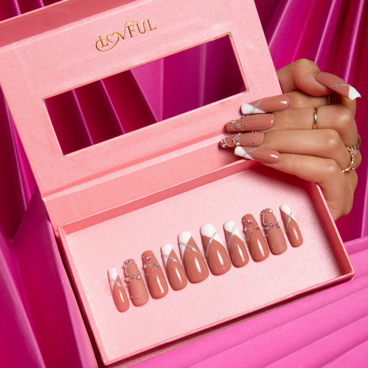 Coffin-shaped press-on nails with a flesh-toned base and white French tips, featuring glitter and studded decorations. Lovful logo on pink box with a window, held against a bright pink background.