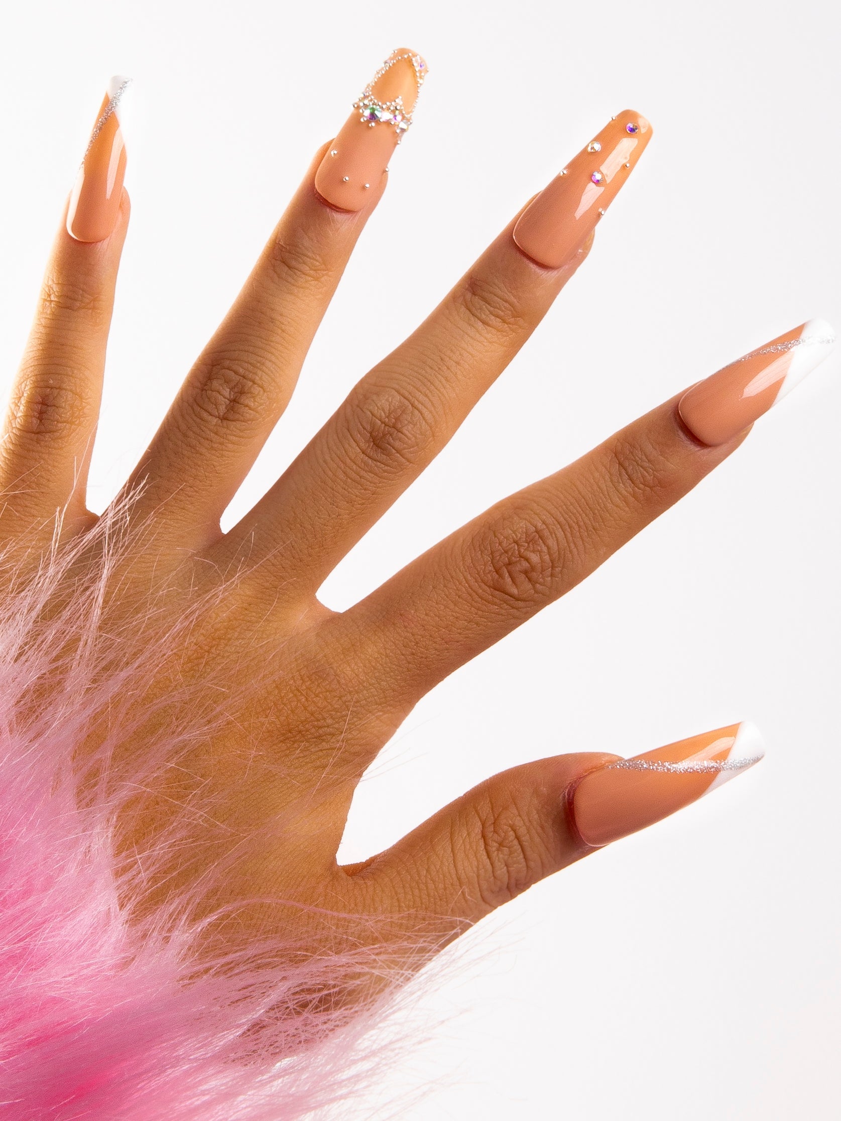 Hand displaying 'Lovely Kitten Heels' press-on acrylic nails with French tips and glitter on a white base, partially wrapped in pink fluffy fabric.