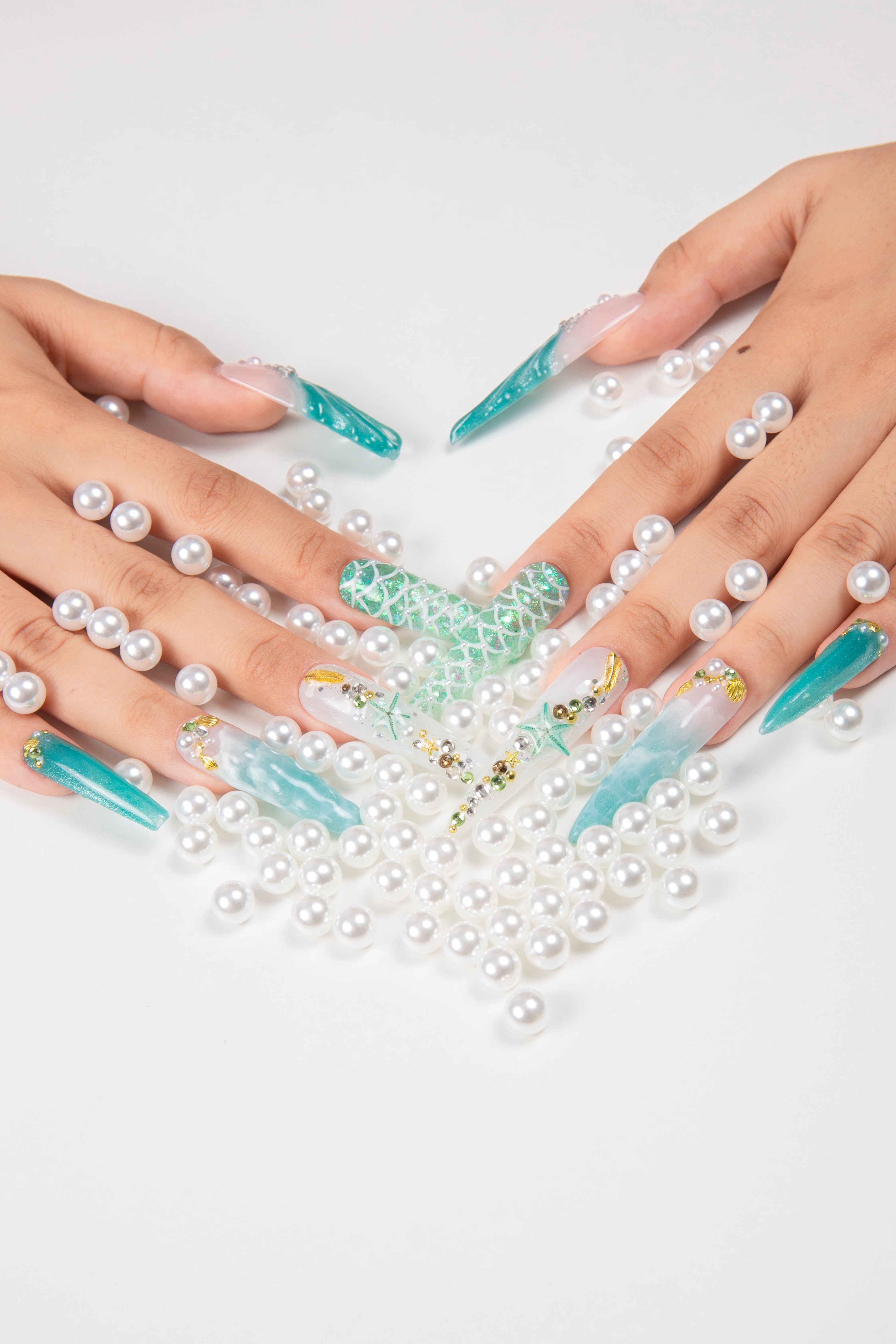 Close-up of hands decorated with Lovful's Surfing Girls blue press-on nails featuring starfish, glitter, and sea-inspired designs, surrounded by white pearls.