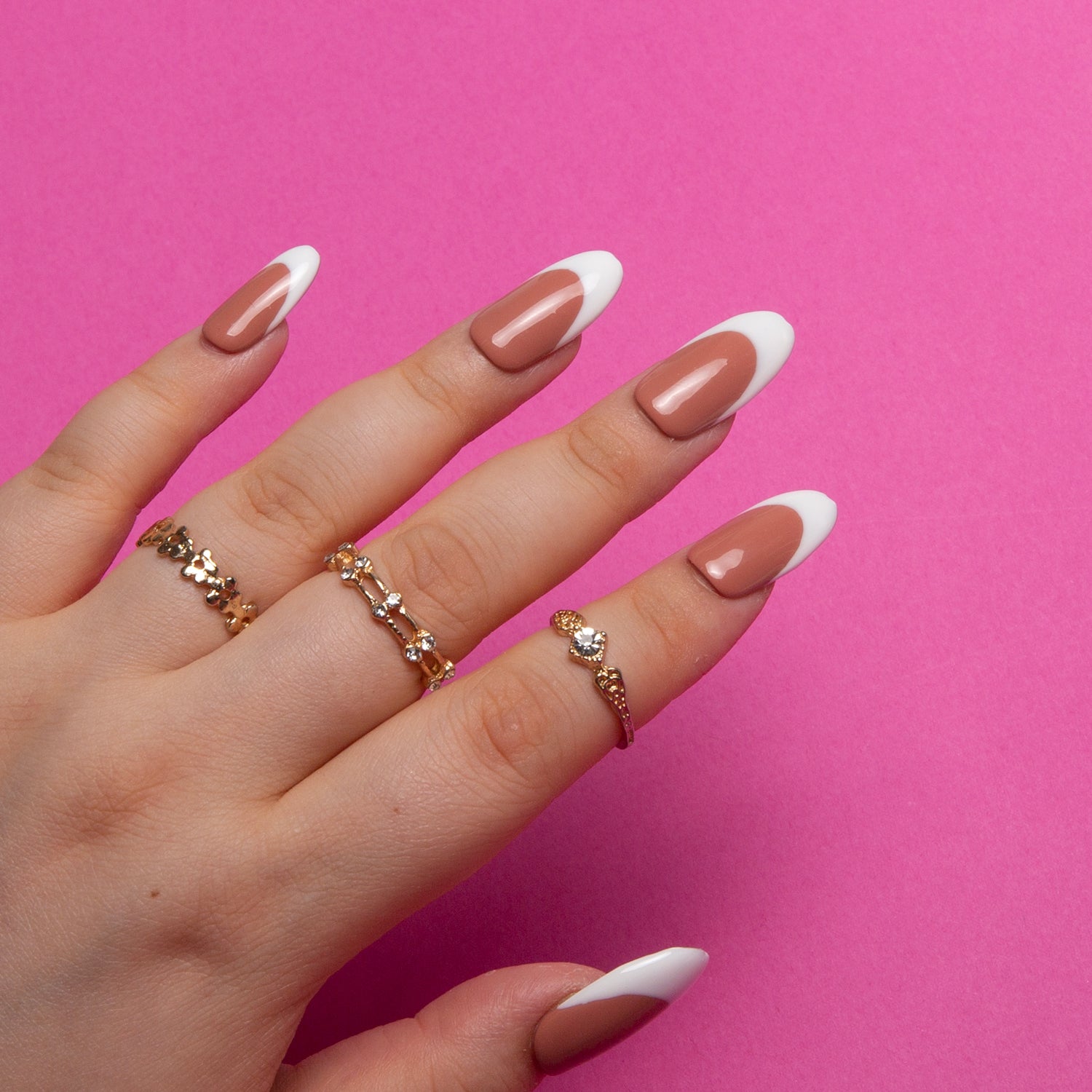Hand with long round Coffee Latte French Tip press-on nails, featuring a rich brown base and white tips, adorned with gold rings against a bright pink background.