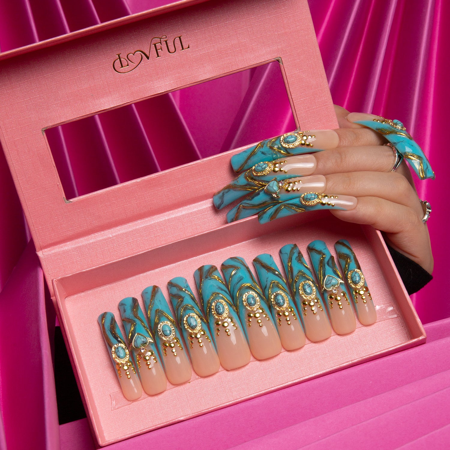 Hand displaying luxurious press-on acrylic nails with turquoise and gold designs, featuring sparkling gems. The nails are placed in a pink Lovful box, perfect for glamorous events.