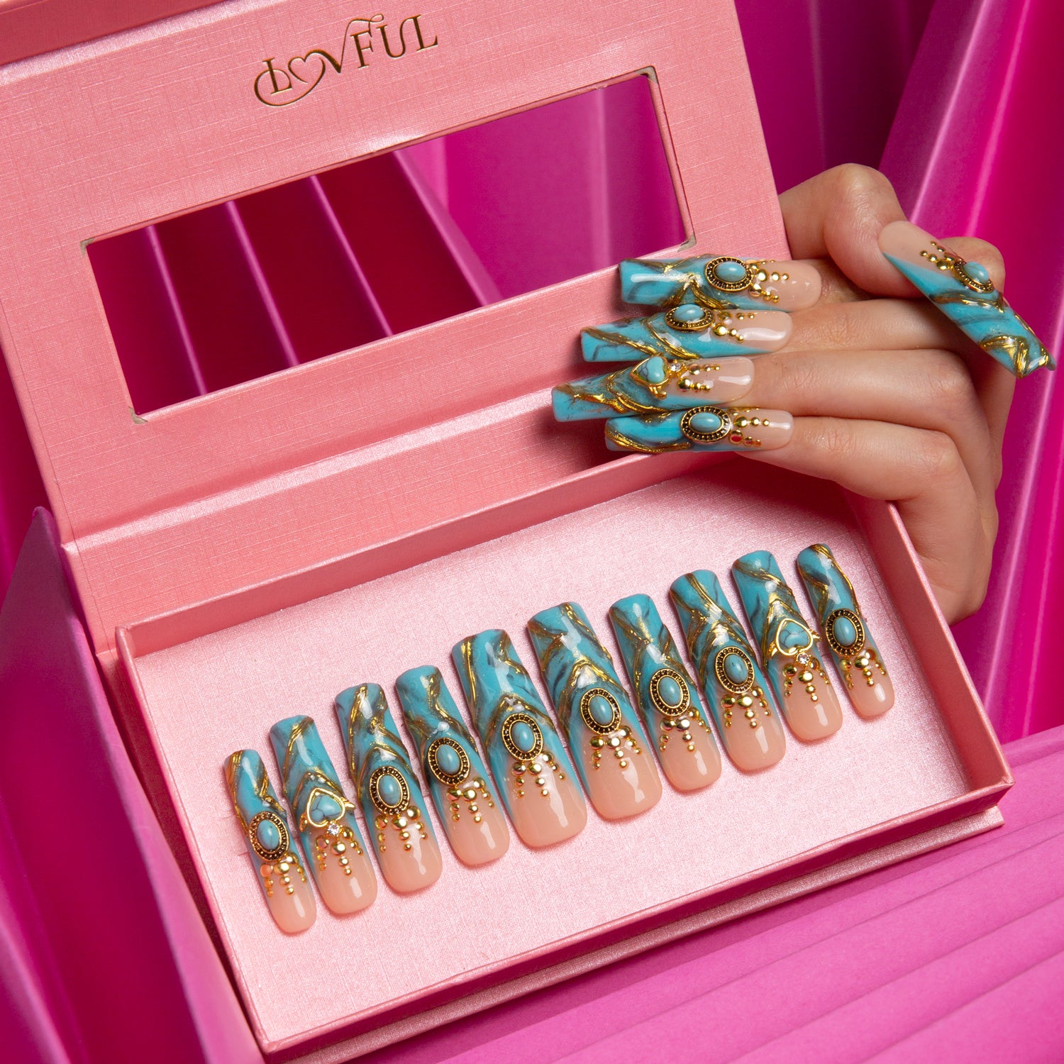 Turquoise and gold press-on acrylic nails in a pink Lovful brand box. The nails are decorated with golden decor and sparkling gems, with a hand holding two nails above the box.