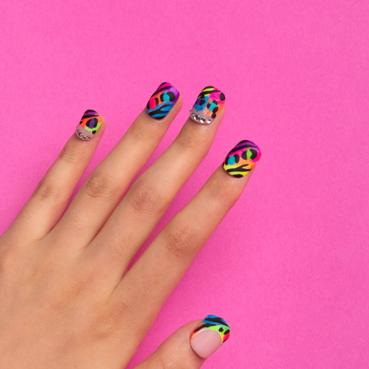 Hand with press-on acrylic nails featuring colorful bright French tips and leopard prints on a pink background