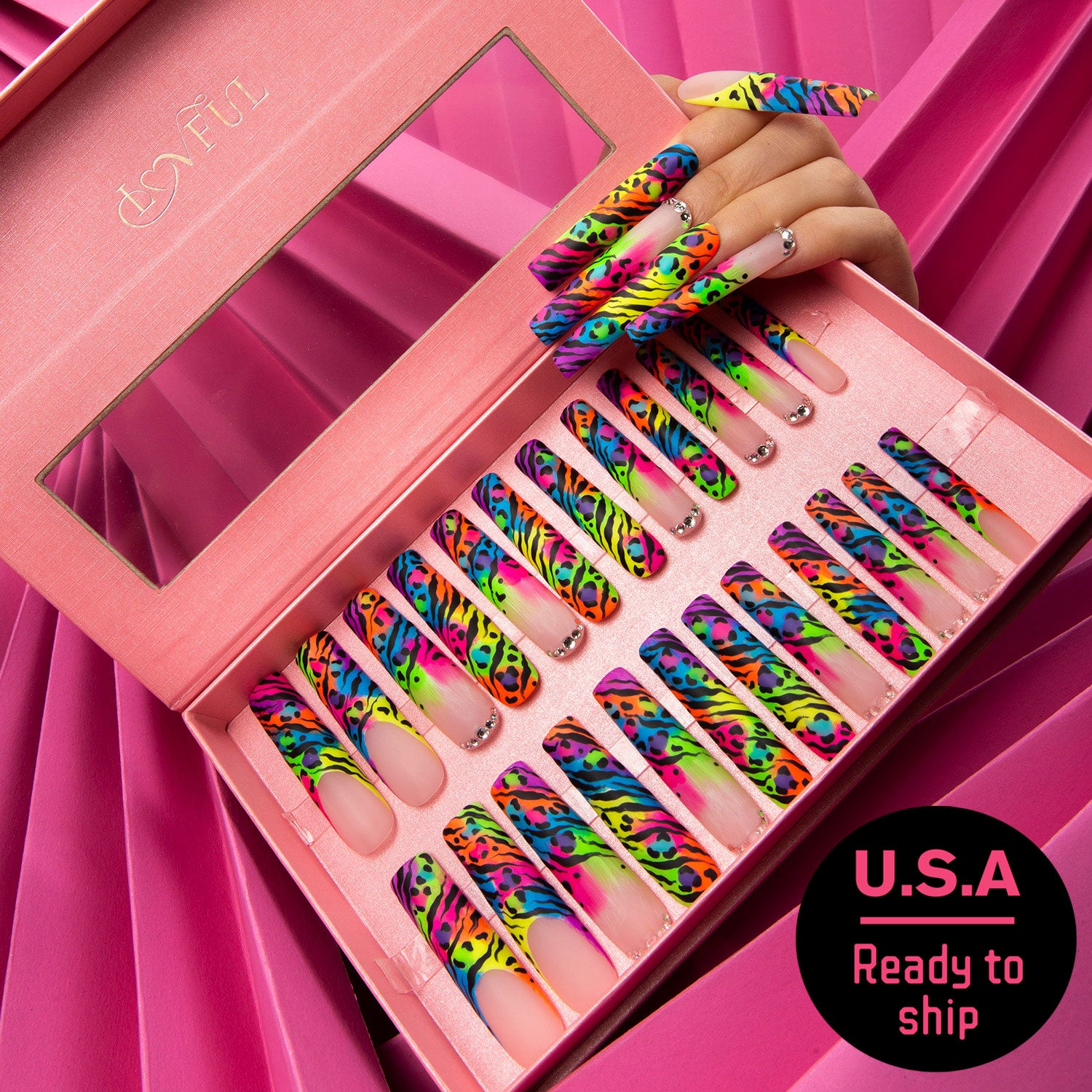 Set of 24 bright colorful press-on nails with leopard prints displayed in a pink Lovful box with a transparent lid against a pink background. A hand with matching nails is shown. Text label reads 'U.S.A Ready to ship'.