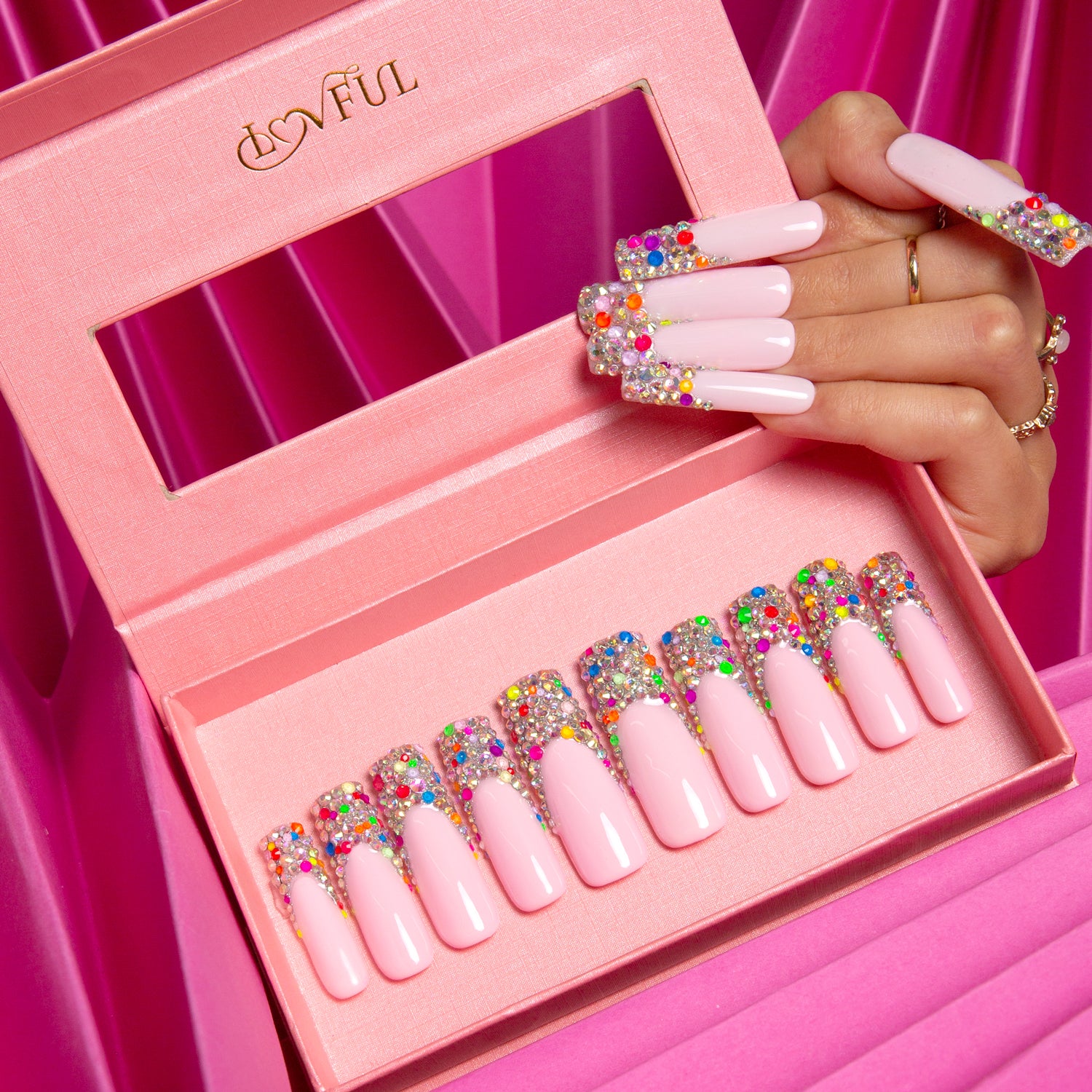 Lovful 'Jelly Bean' press-on nails featuring a nude base with colorful sugary beans on the tips, displayed in a pink box, with a hand holding one nail showcasing its design.