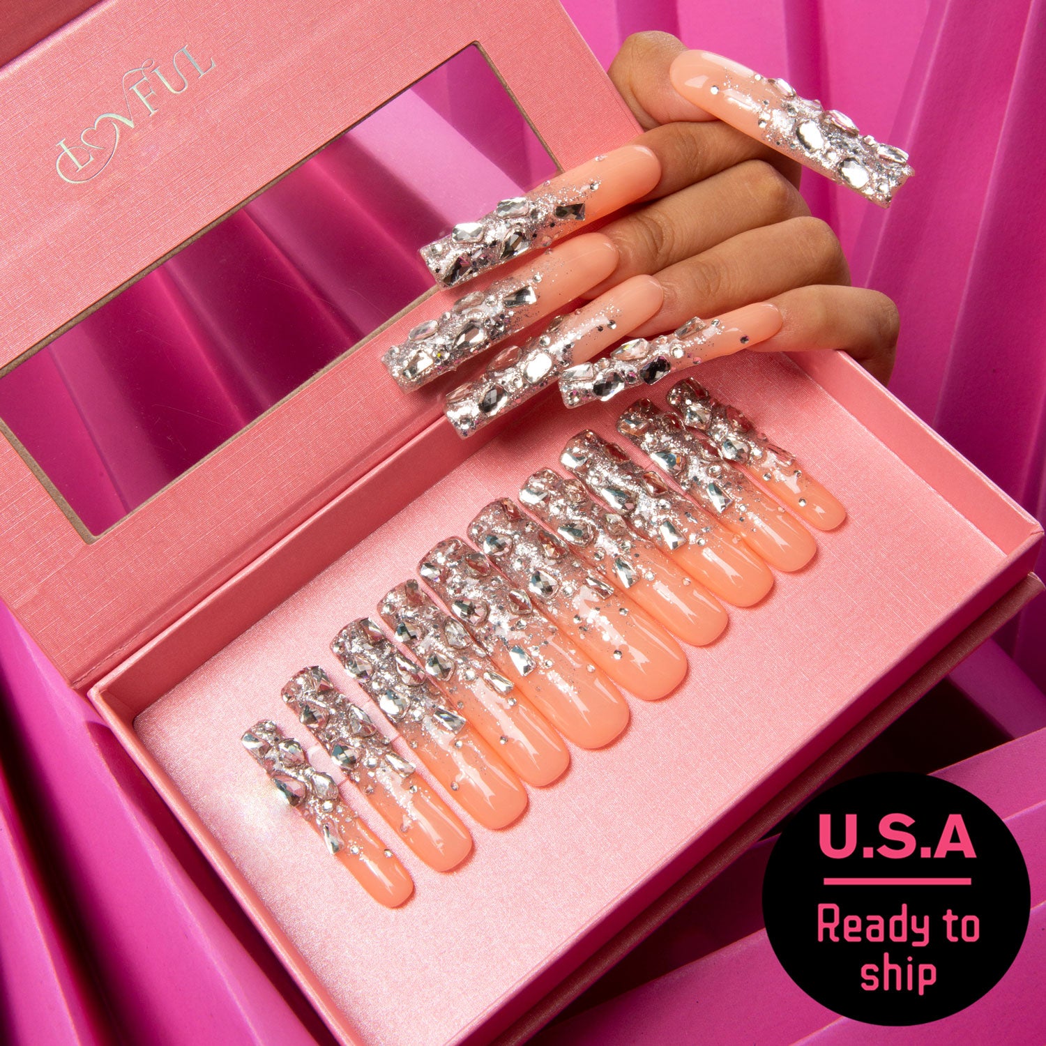 Open pink box containing nude base press-on nails with silver glitter and rhinestones, alongside a hand with similar manicured nails. Includes 'U.S.A Ready to ship' text.