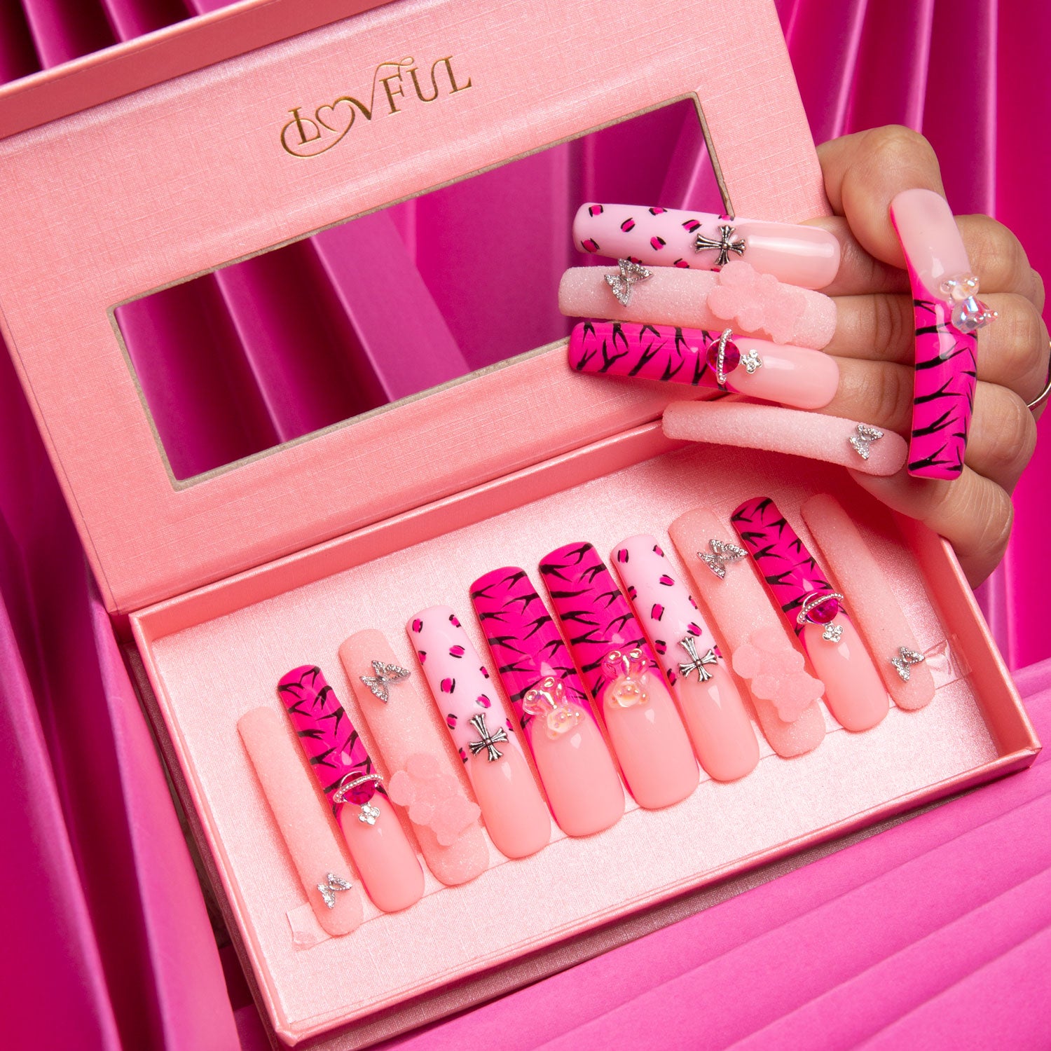 Safari Love Curve press-on nails by Lovful in a pink box with hand-drawn leopard prints, lips, and butterfly accents held by a hand with similar nails.