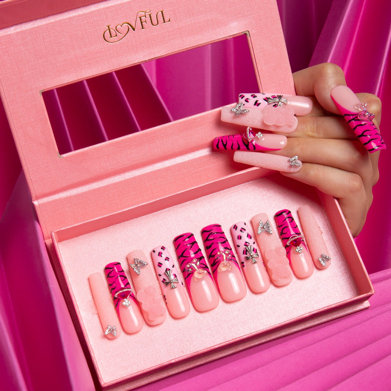 Safari Love press-on nails in pink box, with hot pink French tips, leopard prints, lips and butterfly designs, displayed with a hand holding several nails.
