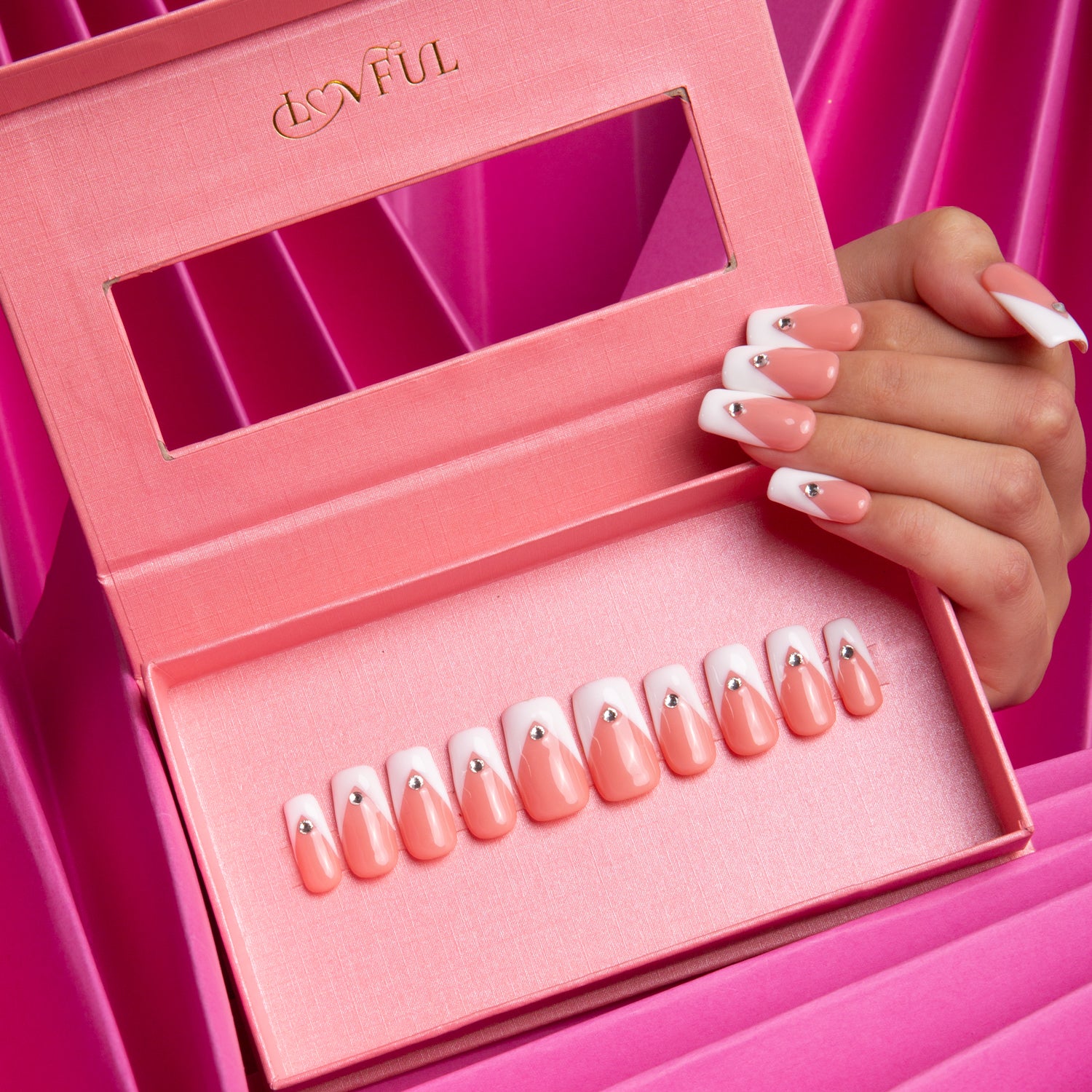 Lovful's Eternal Polaris Press-On Nails displayed in a pink box, featuring white triangle French tips and rhinestones. A hand with the same nail design is shown, set against a pink background.