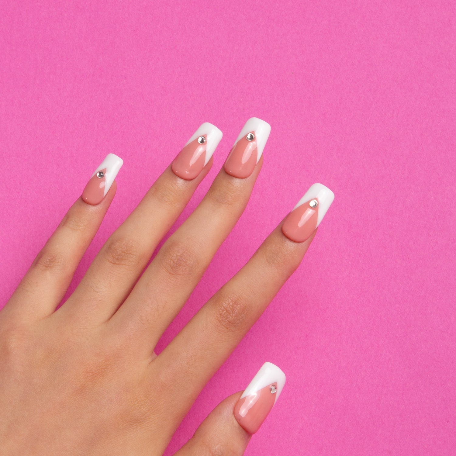 Hand displaying Eternal Polaris press-on nails with white triangle French tips and rhinestones, set against a pink background. Ideal for elegance and sophistication.