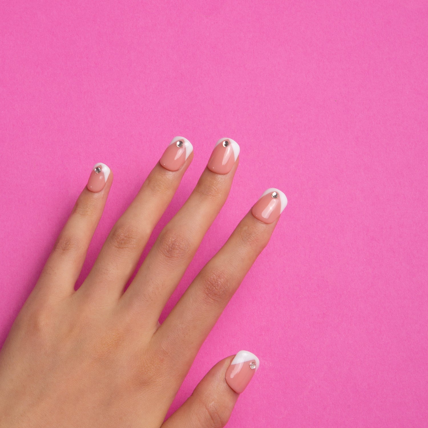 Hand with 'Eternal Polaris' press-on acrylic nails from Lovful on a pink background. The nails have white triangle French tips and are decorated with a single rhinestone on each nail.