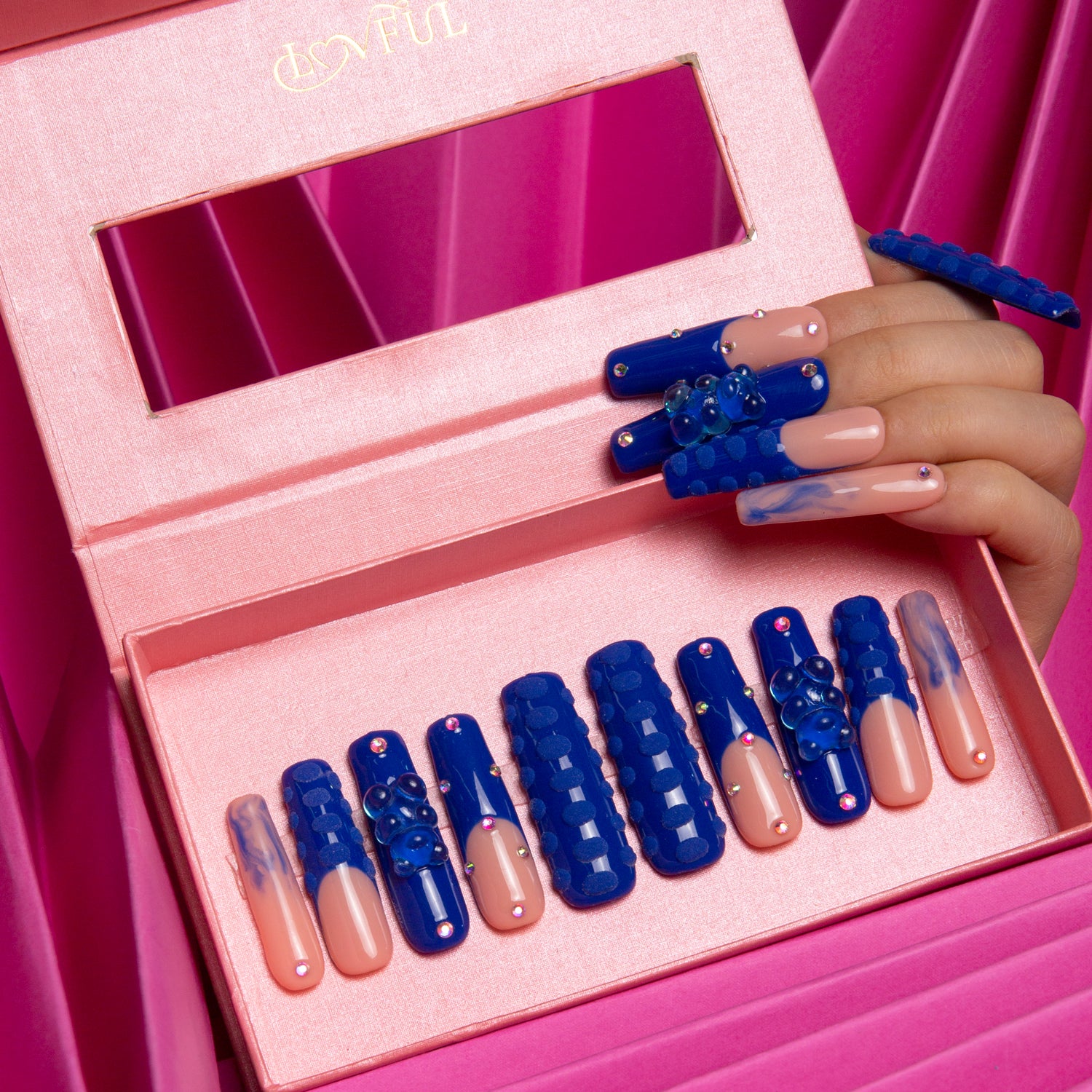 Open pink nail box displaying Little Blue Bear press-on acrylic nails with blue gummy bear patterns, rhinestones, and 3D dots on a pink satin background.