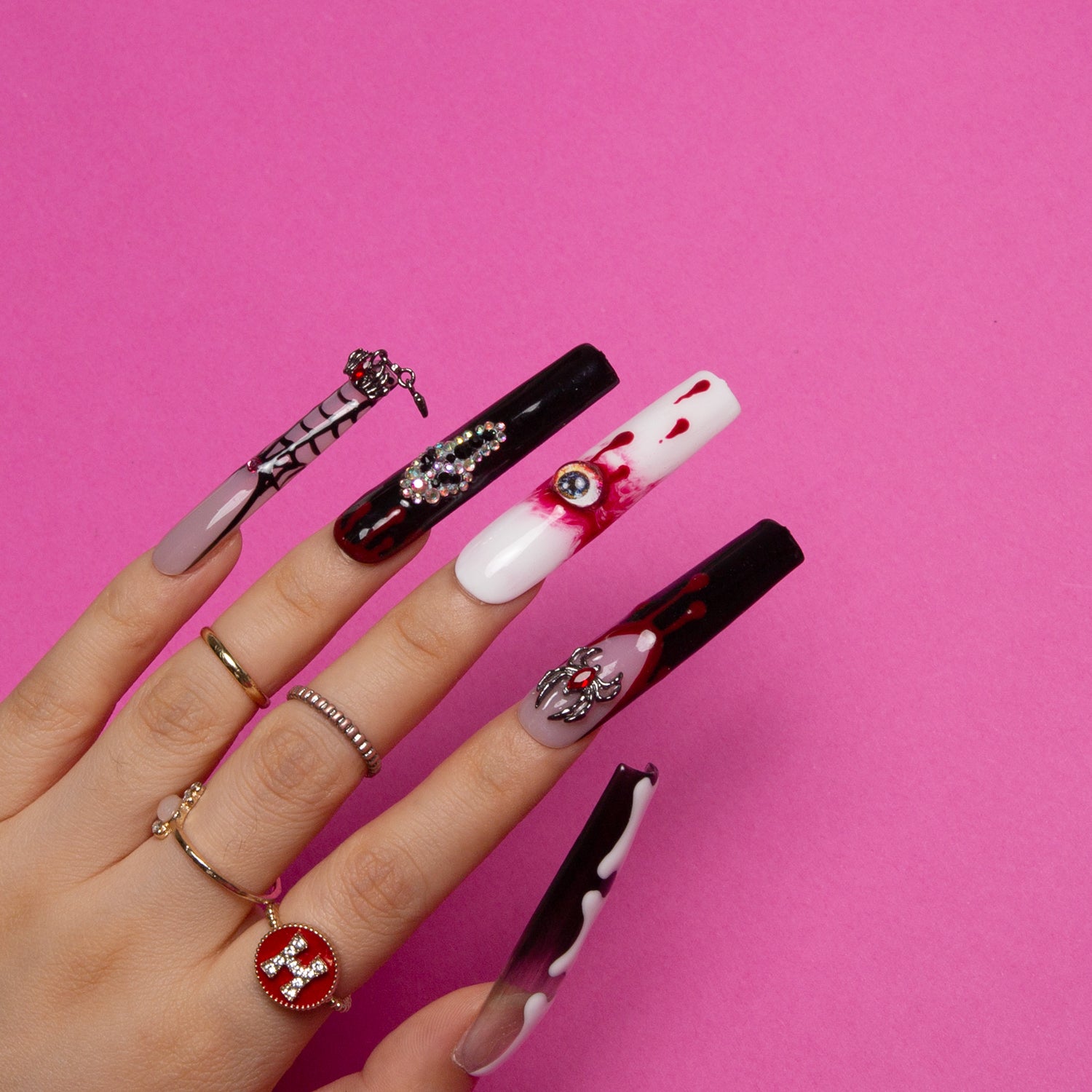 Hand with 'Final Destination' press-on acrylic nails in bold red and black hues. The nails feature spooky designs including eyes, ghosts, and bone patterns. Square-shaped nails with a macabre theme, perfect for Halloween.