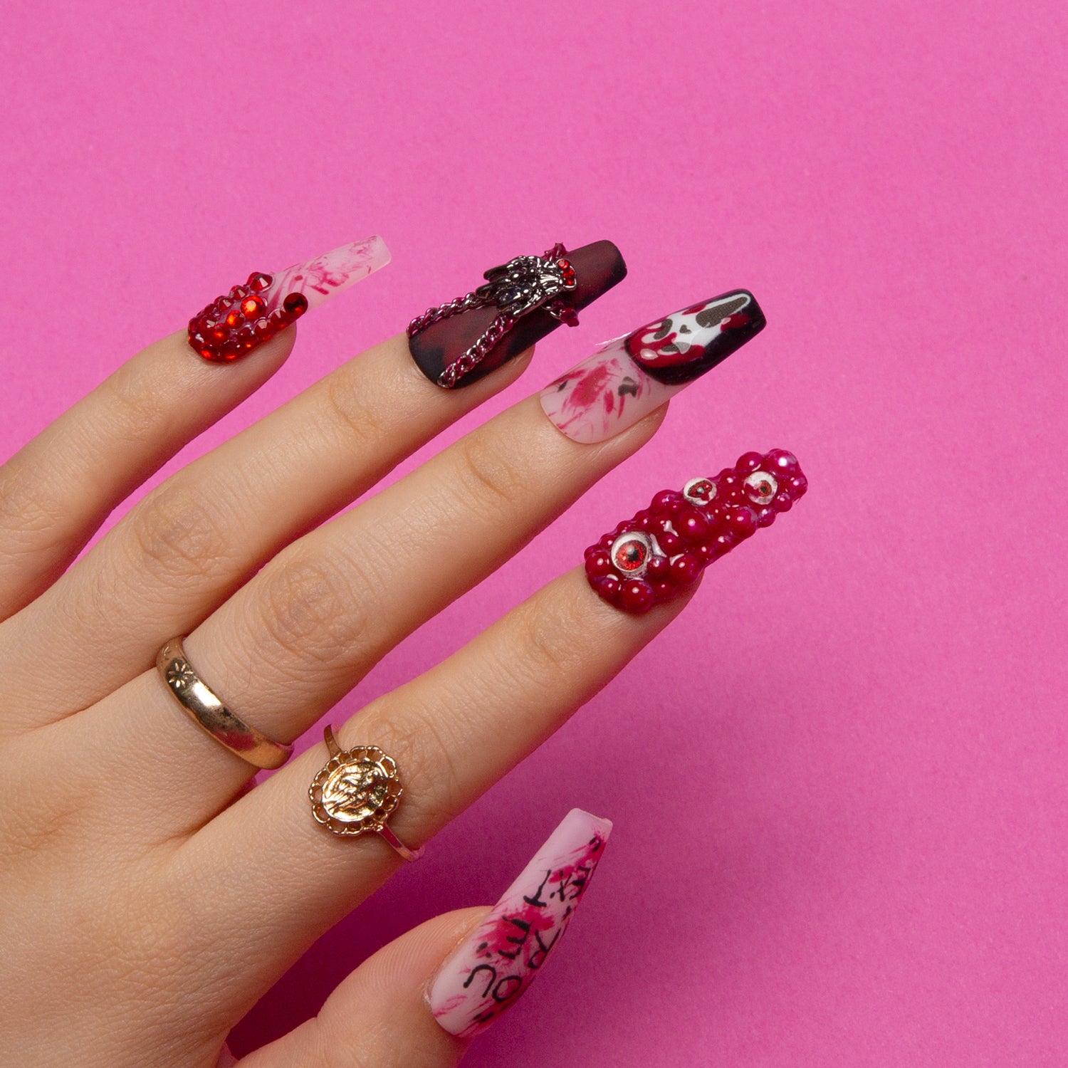 Hand wearing 'You Are Next' press-on nail set with ghostface design, eerie eyes, and blood-red splashes on coffin-shaped nails. Nails have 3D embellishments and Halloween-themed prints on a bright pink background.