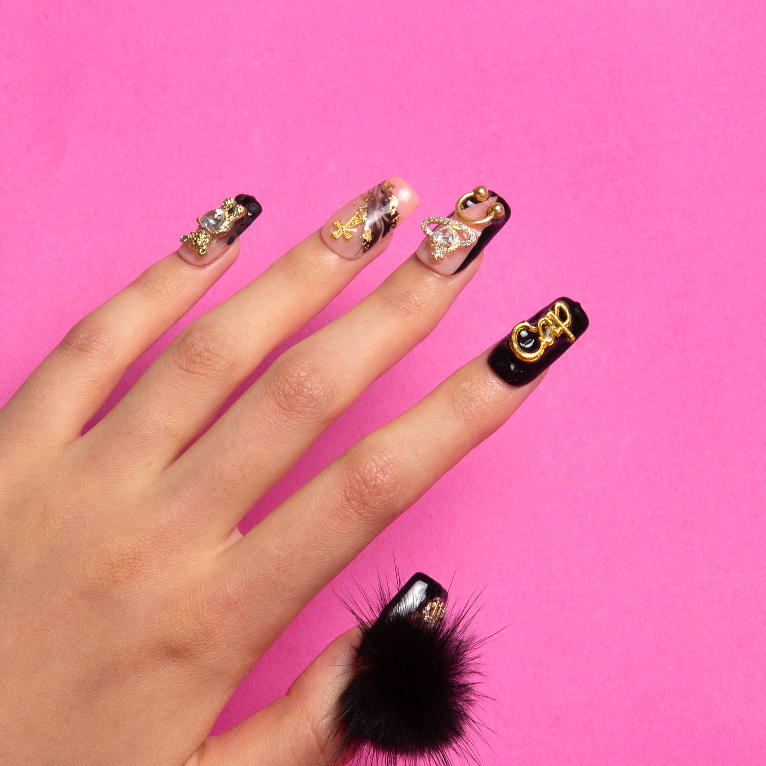 Hand with black and white Capricorn zodiac press-on nails adorned with gold decorations and detachable fluffy balls.