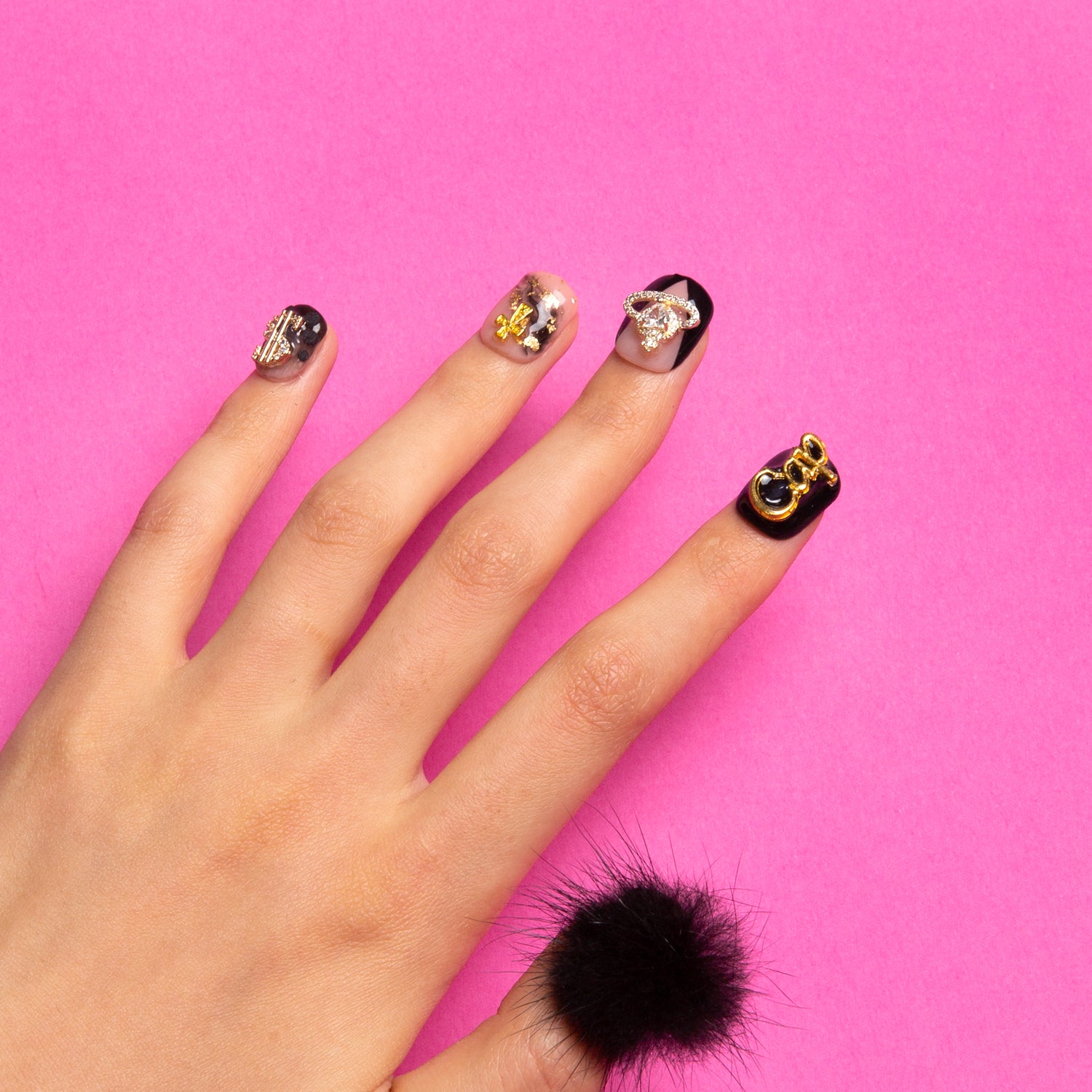 Capricorn-themed press-on nails with black and white design, golden decorations, and black fluffy ball against a pink background