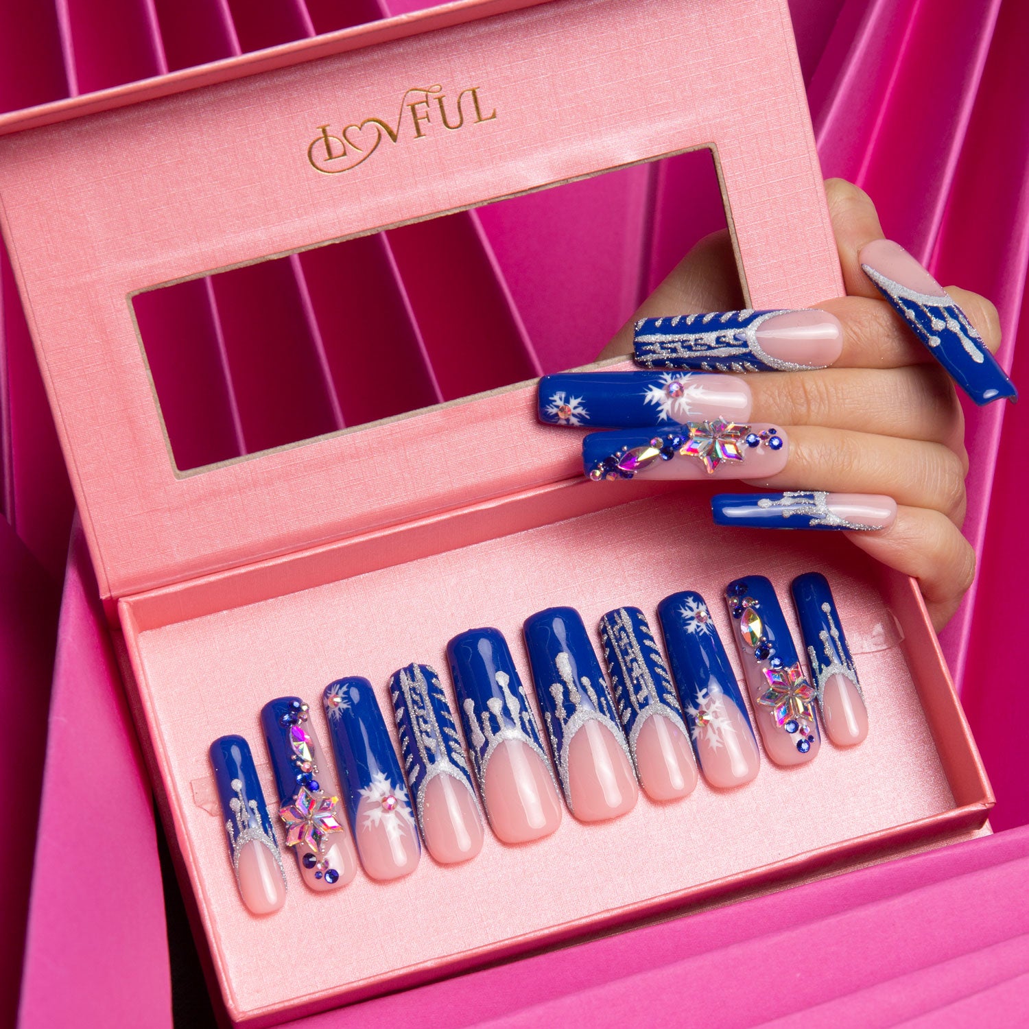 Set of blue French tip press-on nails with white snowflake designs in a pink Lovful box, with a hand model showcasing the nails against a pink background