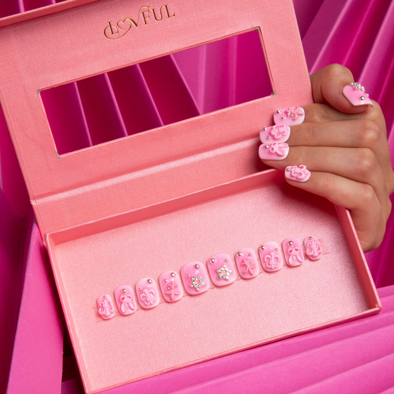 Lovful Pink Bliss Blush press-on nails set with 3D decorations including crosses, hearts, and cat designs, displayed in a branded box held by a hand.