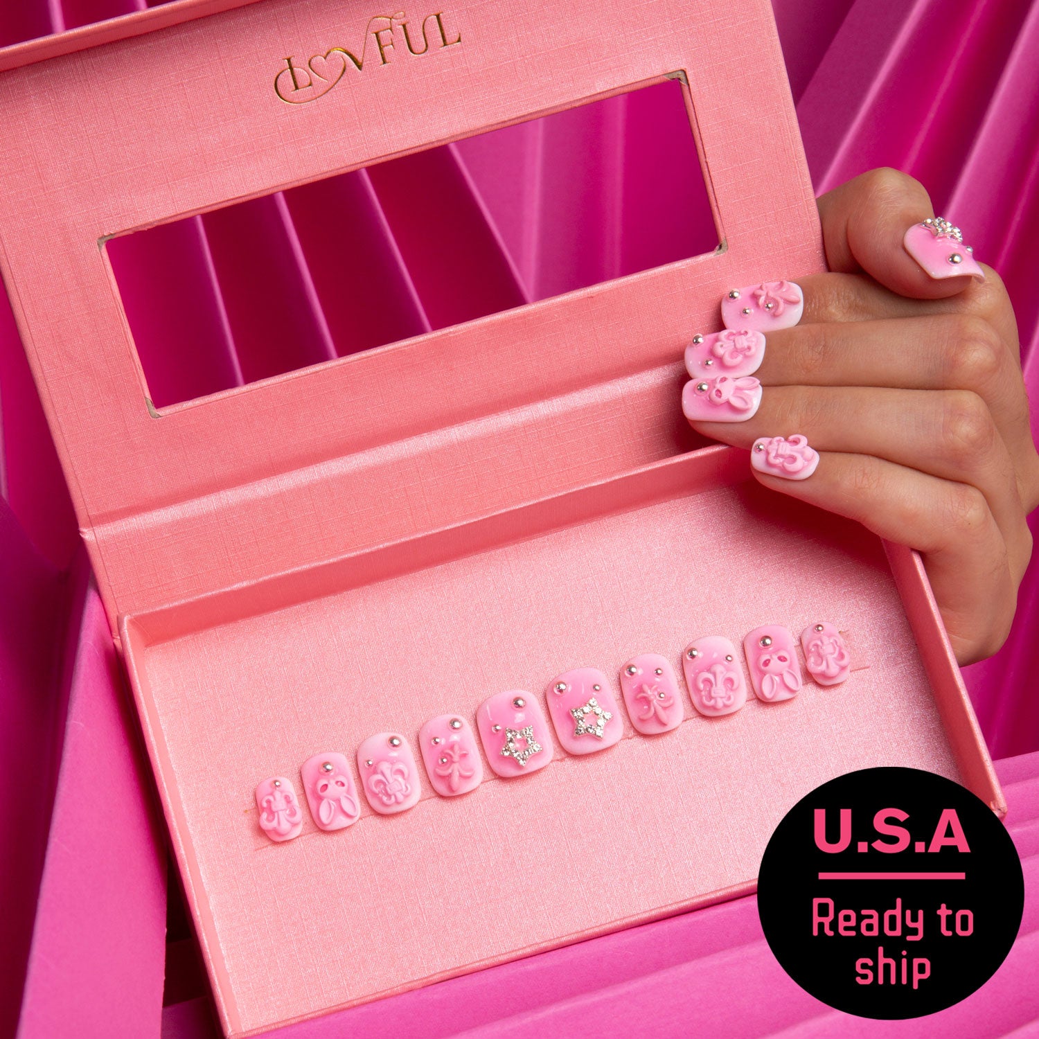 Pink Bliss Blush press-on nails featuring gradient from pink blush to softer shade with pink crosses, cat designs, heart shapes, and planet motifs. Hand showcasing applied nails. Pink box with Lovful logo and 'U.S.A Ready to ship' text.