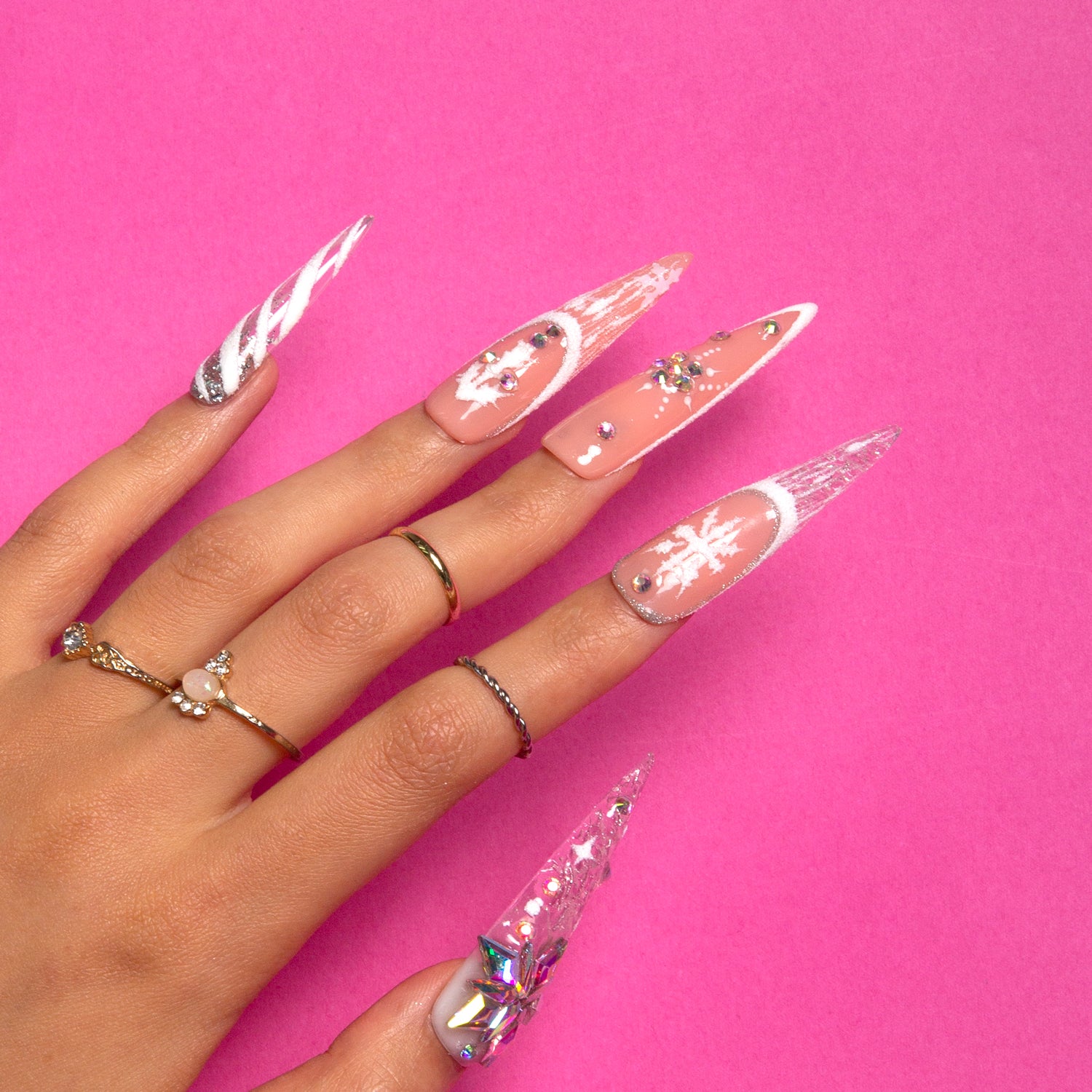 Hand with Lovful's Snowy Moonlight stiletto press-on nails featuring white snowflakes and sparkling accents against a pink background.