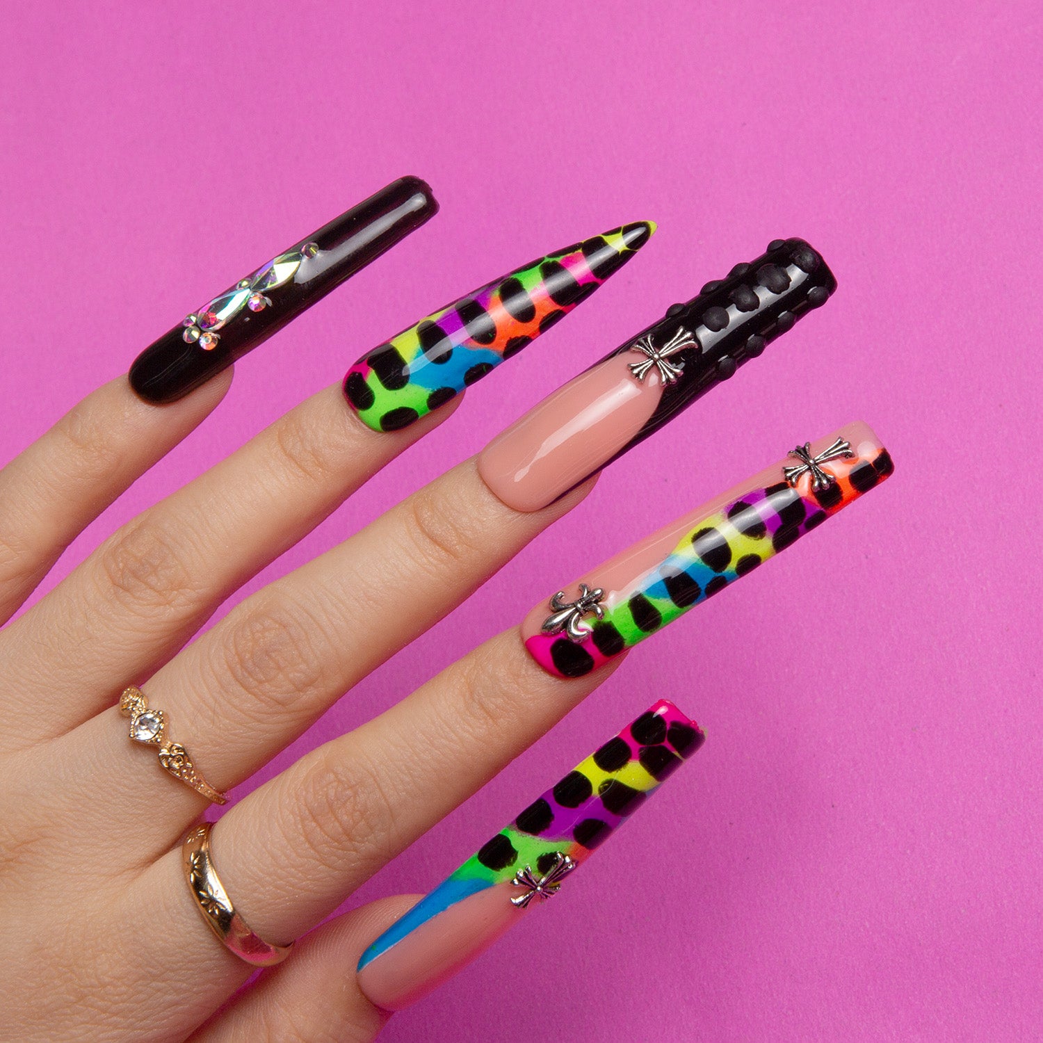 Hand with 'Young Forever' press-on nails featuring black French tips, vibrant rainbow animal prints, and flower rhinestone embellishments against a pink background.