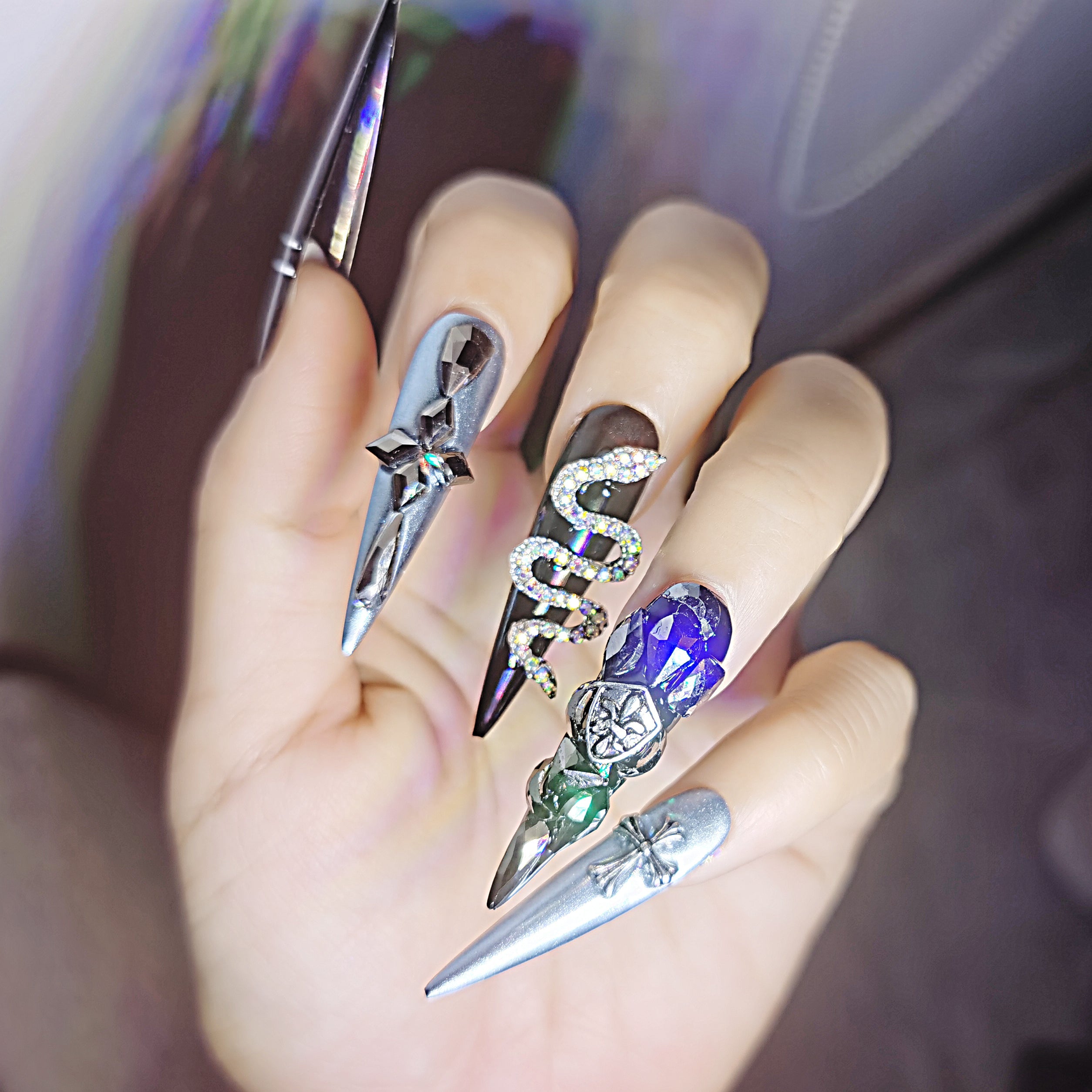 Hand wearing 'Locomotive Girl' press-on nails with a glossy black base, mirror effect, black rhinestones, metallic designs, and gemstone decorations.