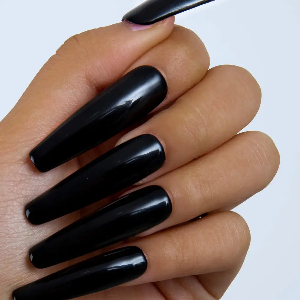 Hand with long, sleek, and shiny black press-on acrylic nails with a glossy finish, reflecting light for an urban chic look.