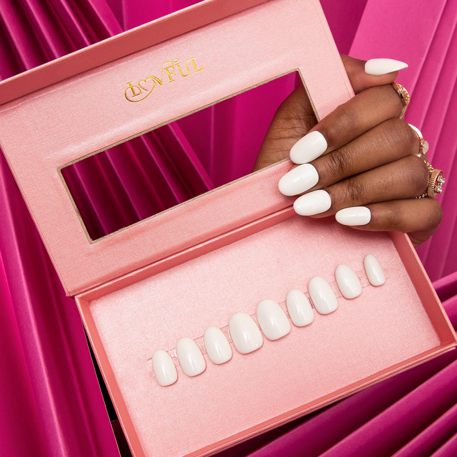 Set of white press-on acrylic nails in a pink Lovful box on a hand with a pink and purple background. Lovful logo displayed in gold on box lid.