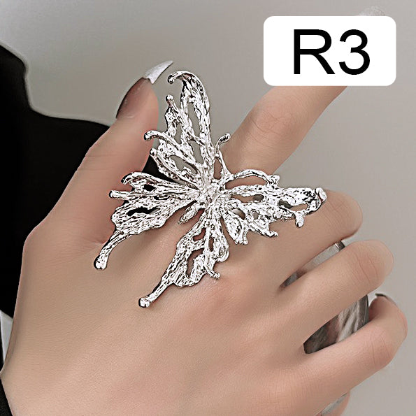 Hand with stylish nails wearing a large silver butterfly-shaped metal ring labeled R3