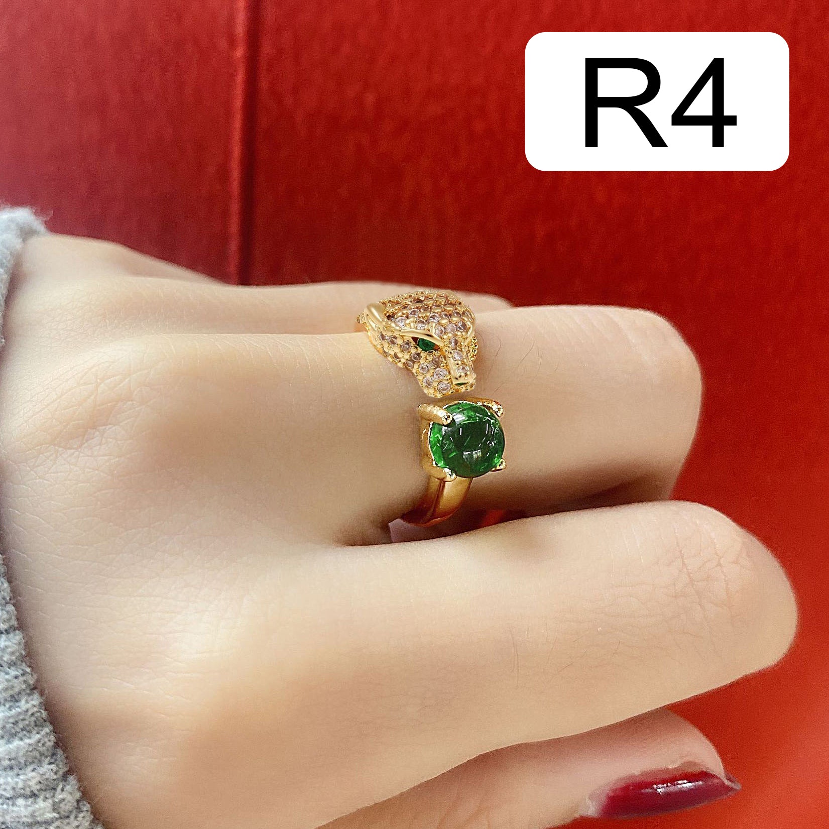 Gold snake-shaped adjustable ring with diamond accents and green gemstones, worn on a hand with a red background. Text in the top right corner reads 'R4'.